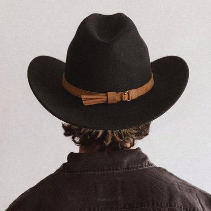 Person wearing a black cowboy hat with a brown band on a plain background
